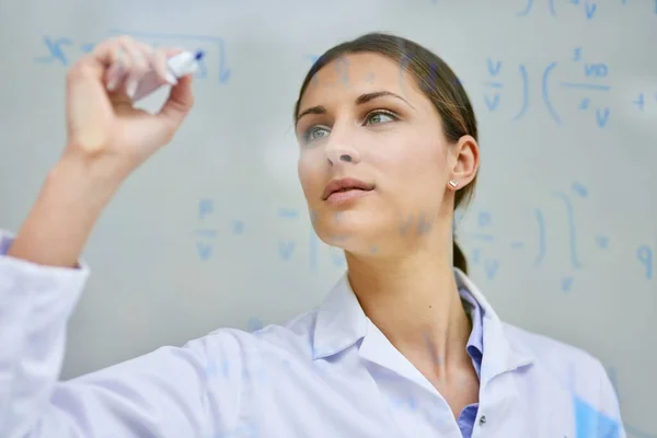 Resolvendo equações para encontrar todas as soluções que ela precisa. Tiro recortado de uma jovem cientista a escrever equações numa parede de vidro num laboratório. — Fotografia de Stock