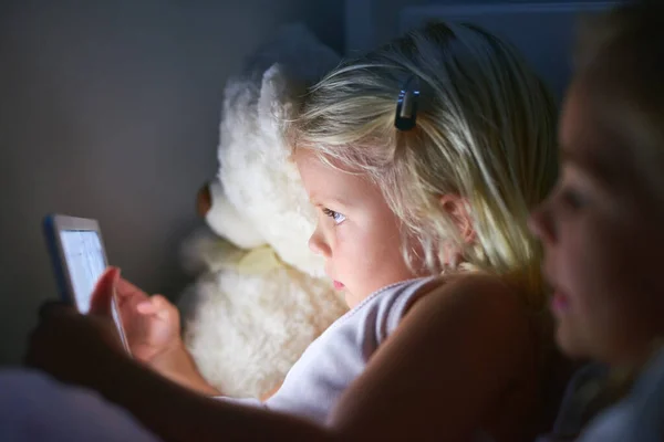 Czas spać stał się o wiele bardziej interaktywny. Zdjęcia dwóch małych dziewczynek korzystających z tabletu cyfrowego przed snem. — Zdjęcie stockowe