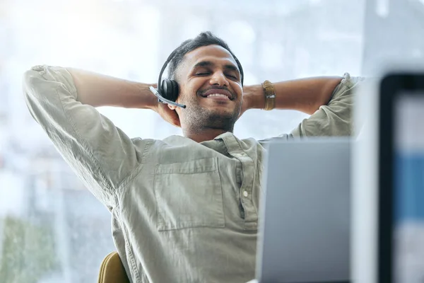 That feeling of overcoming a challenge. Shot of a handsome young salesman sitting alone in his office and feeling successful while wearing a headset. — Stock Photo, Image