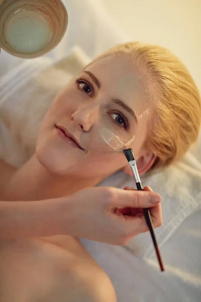 Maintenant tu connais mon secret pour avoir une peau éclatante. Portrait d'une jeune femme recevant un soin du visage dans un spa. — Photo