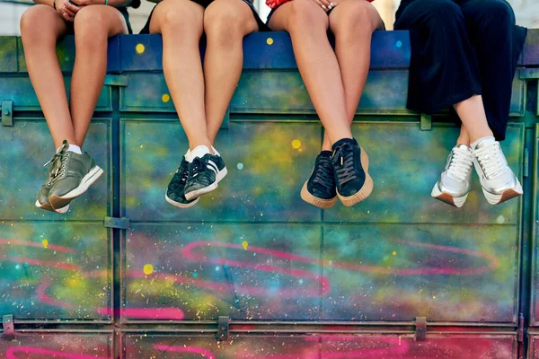 Sätt dig. Beskuren bild av fyra oigenkännliga flickvänner som sitter på en graffitivägg i staden. — Stockfoto