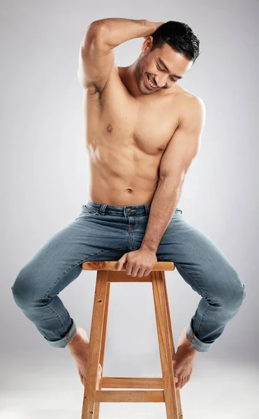 Sterke buikspieren voor een zacht hart. Studio shot van een knappe jonge man pronken met zijn gespierd lichaam terwijl zitten op een stoel tegen een grijze achtergrond. — Stockfoto
