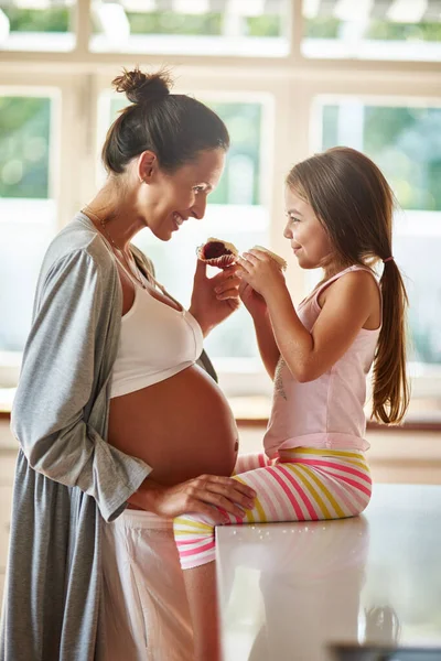 Ik deel wat zoete lekkernijen samen. Shot van een zwangere vrouw en jong meisje samen cupcakes eten. — Stockfoto