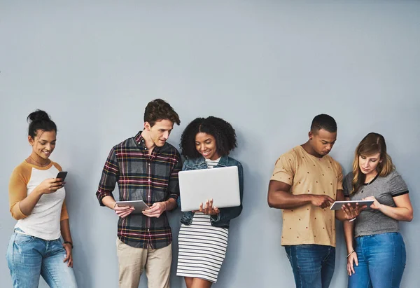 Ik heb alles wat er nu is gebruikt. Studio shot van een groep jongeren met draadloze technologie tegen een grijze achtergrond. — Stockfoto