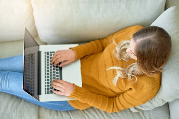 Conectado al mundo desde la comodidad del hogar. Foto de ángulo alto de una mujer joven usando su computadora portátil mientras está sentada en el sofá en casa. —  Fotos de Stock