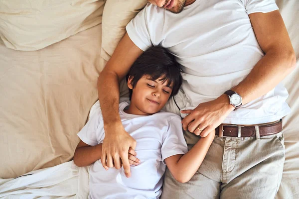 Určitě bude mít nějaké sladké sny. Vysoký úhel záběru malého chlapce spí vedle svého otce v posteli doma. — Stock fotografie