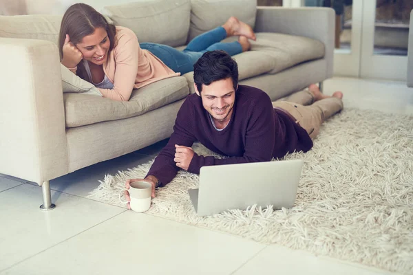 De älskar att vara online tillsammans. Skjuten av ett leende ungt par med hjälp av en bärbar dator medan du kopplar av i deras vardagsrum. — Stockfoto