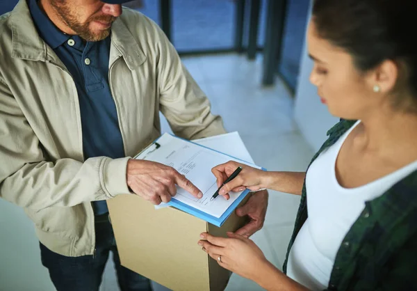 Su firma aquí ruega, señora. Fotografía de una joven firmando por un paquete de un repartidor. —  Fotos de Stock