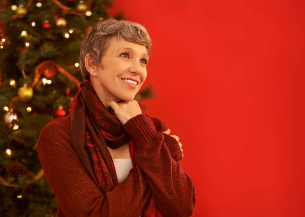 Είναι η εποχή της χαράς. Μια χαρούμενη ώριμη γυναίκα που δείχνει στοχαστική μπροστά σε ένα χριστουγεννιάτικο δέντρο.. — Φωτογραφία Αρχείου