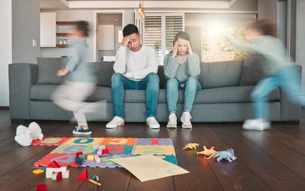 Need a break. Shot of two young parents looking tired while their children run around at home. — Stock Photo, Image