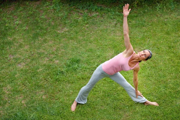 Ejercicio relajante. Tiro de una mujer madura haciendo la pose de yoga triangular extendido al aire libre. — Foto de Stock