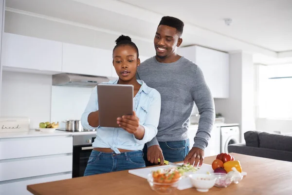 Você não pode dar errado com uma receita passo a passo. Tiro de um casal olhando para algo em um tablet digital enquanto cozinha. — Fotografia de Stock