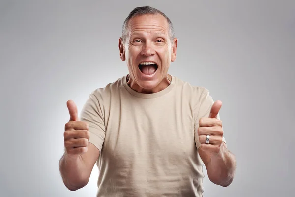 Ça ne peut pas aller mieux qu'un double pouce. Prise de vue d'un bel homme mature debout sur un fond gris dans le studio et faisant un geste pouce vers le haut. — Photo