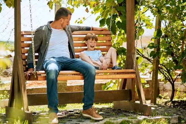 Tempo, o maior presente para dar a uma criança. Tiro de um pai e seu filho adorável relaxando juntos em um balanço de jardim. — Fotografia de Stock