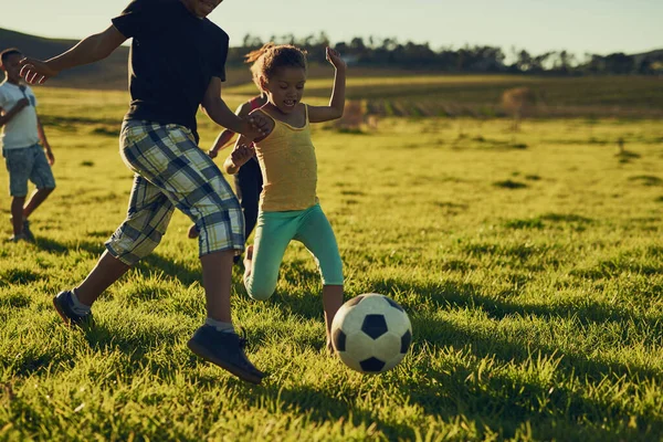 Plezier met vrienden en een voetbal. Schot van een groep kinderen die samen voetballen in een veld buiten. — Stockfoto