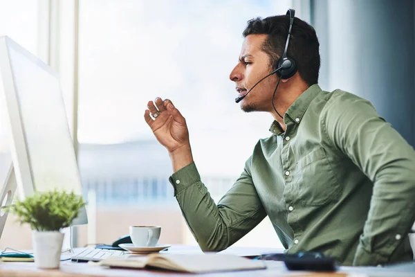 Hij geeft het beste financiële advies. Shot van een zelfverzekerde jonge zakenman pratend door een headset terwijl hij aan zijn bureau zit in het kantoor. — Stockfoto