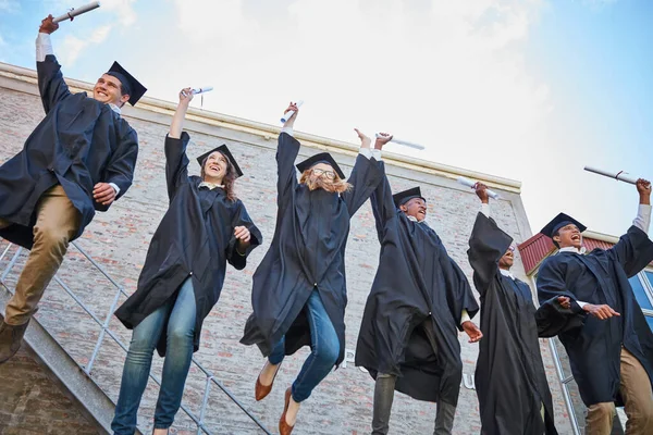 A diplomaosztó ok az ünneplésre. Alacsony szög lövés egy boldog csoport diákok ugrás ünneplés a diplomaosztó napján. — Stock Fotó