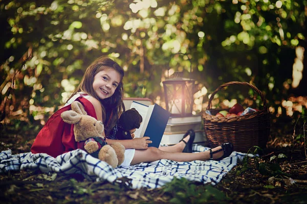 Pouvez-vous deviner quelle est mon histoire préférée. Portrait d'une petite fille lisant un livre avec ses jouets dans les bois. — Photo