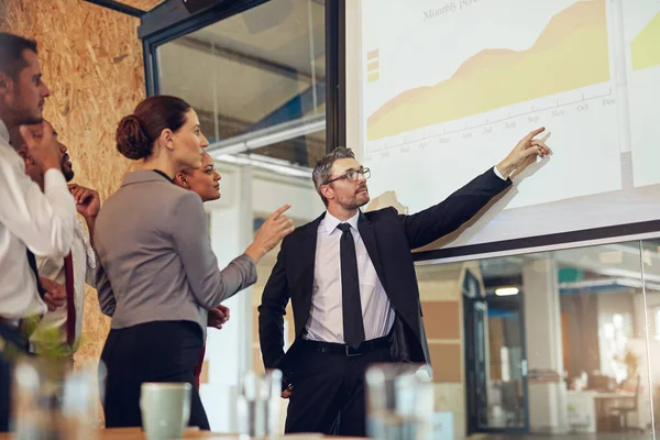 Rennt mit seinem Team durch die Zahlen. Aufnahme einer Führungskraft bei einer Präsentation auf einer Projektionswand vor einer Gruppe von Kollegen in einem Sitzungssaal. — Stockfoto