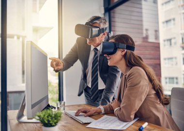 Fikirlerini yeni boyutlara aktarıyorlar. Ofisteki bilgisayarda çalışırken VR kulaklık takan iki iş adamının fotoğrafı..