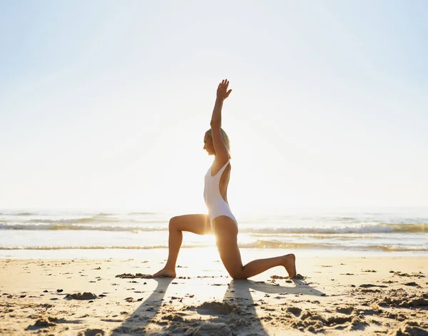 Empezando el día de la manera correcta. Largura completa de una atractiva joven haciendo yoga temprano en la mañana en la playa. — Foto de Stock