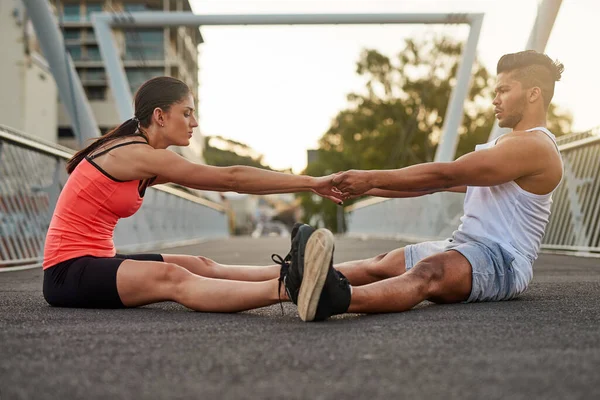 Deixa-me ajudar-te. Tiro de um jovem casal aquecendo em uma ponte antes de seu treino. — Fotografia de Stock