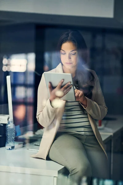 Sempre conectado às últimas atualizações de negócios. Tiro de uma jovem empresária usando um tablet digital durante uma noite no trabalho. — Fotografia de Stock
