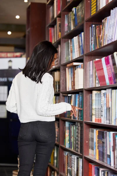 Sto cercando la sua prossima lettura interessante. Girato di una giovane donna che naviga libri su uno scaffale in una biblioteca. — Foto Stock