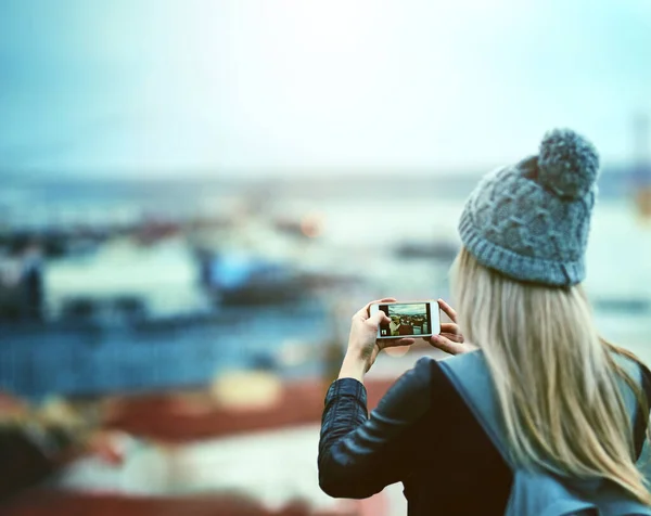 Ze verzamelt herinneringen. Achteraanzicht foto van een jonge vrouw met behulp van een mobiele telefoon om foto 's van een stad uitzicht te nemen. — Stockfoto