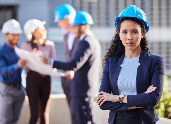 Mon équipe peut gérer n'importe quoi. Prise de vue d'une jeune femme d'affaires debout les bras croisés et portant un casque tandis que ses collègues se tiennent derrière elle. — Photo