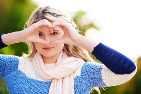 Der Blick der Liebe. Ausgeschnittenes Porträt einer jungen Frau, die durch ihre Hände schaut, während sie im Freien eine Herzform herstellt. — Stockfoto