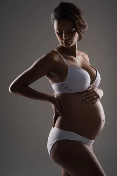 A kötelék a baba születése előtt kezdődik. Stúdió lövés egy gyönyörű fiatal terhes nő pózol fehérneműben szemben szürke háttér. — Stock Fotó