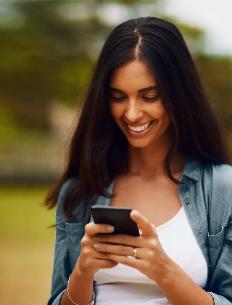 Wat iedereen van plan is dit weekend. Foto van een aantrekkelijke jonge vrouw met behulp van een mobiele telefoon in een park. — Stockfoto