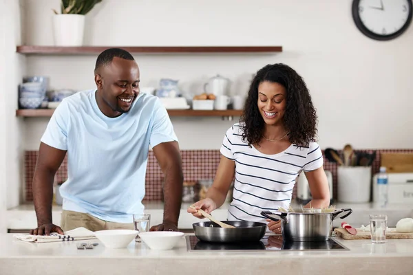 Han elsker å se henne lage mat. Et bilde av et ungt ektepar som lager mat sammen på kjøkkenet hjemme. – stockfoto
