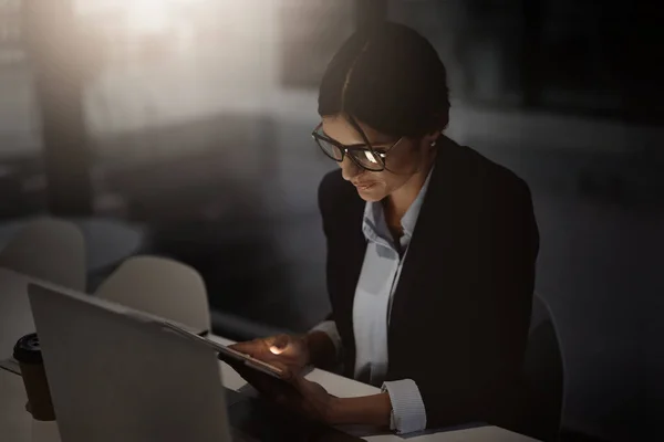 Reste tard, reste au travail. Prise de vue d'une jeune femme d'affaires utilisant une tablette numérique et un ordinateur portable tard dans la nuit dans un bureau moderne. — Photo