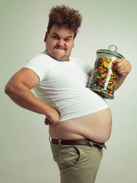 This will help me grow nice and big. Cropped shot of an overweight man holding a large jar of candy. — Stock Photo, Image