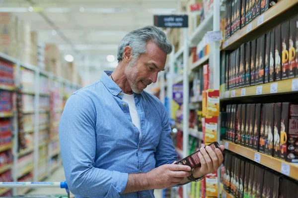 Se ve bien, lo compraré. Tiro de un hombre maduro guapo leyendo la etiqueta en una caja mientras hace compras en una tienda de comestibles. —  Fotos de Stock