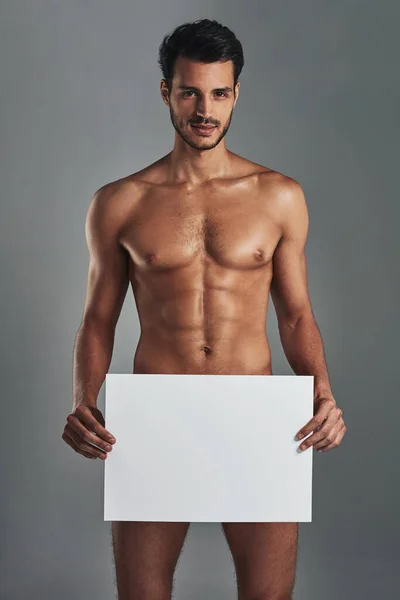 Znamení pro citlivá témata. Studio záběr pohledný a svalnatý mladý muž drží prázdný znak na šedém pozadí. — Stock fotografie