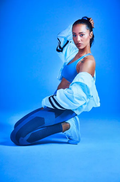Fitness benim dinim. Mavi arka planda dizlerinin üzerinde poz veren çekici genç bir bayan sporcunun tam boy portresi.. — Stok fotoğraf