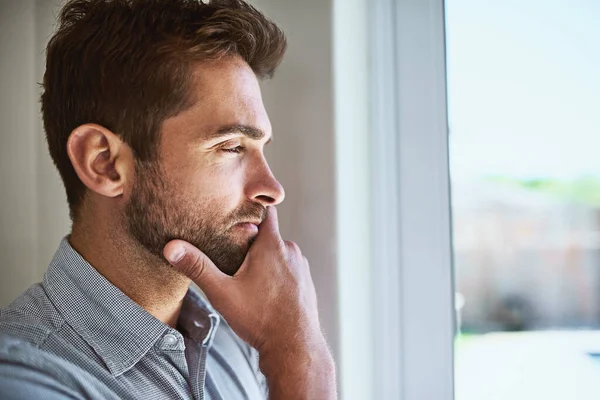 A cosa sta pensando? Girato di un giovane focalizzato guardando attraverso una finestra mentre contemplava dentro casa durante il giorno. — Foto Stock