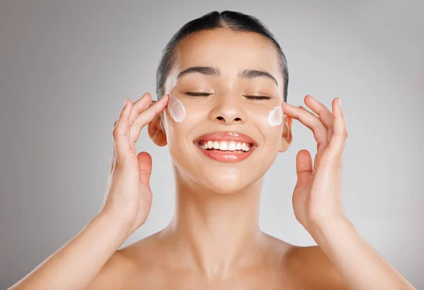 Me encanta cómo mi piel la regala. Foto de estudio de una atractiva joven que se aplica crema hidratante en la cara sobre un fondo gris. —  Fotos de Stock