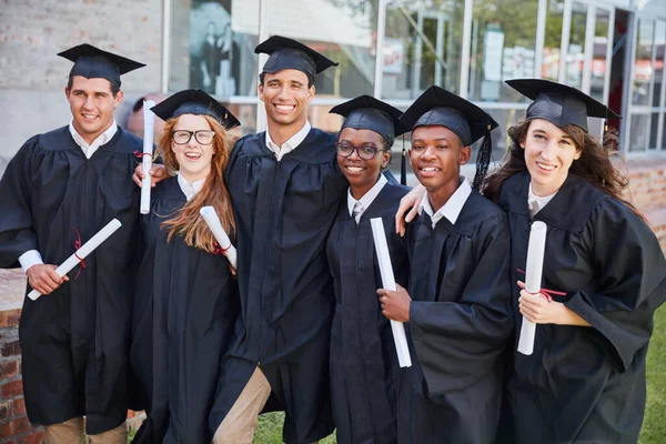 Maintenant, nous pouvons nous appeler diplômés. Portrait d'un heureux groupe d'étudiants debout à l'extérieur le jour de leur graduation. — Photo
