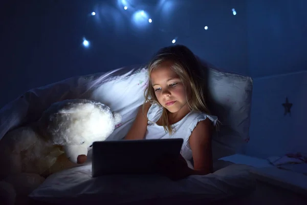 Ciekawi mnie nowoczesna technologia. Strzał dziewczynki używającej tabletu cyfrowego przed snem. — Zdjęcie stockowe