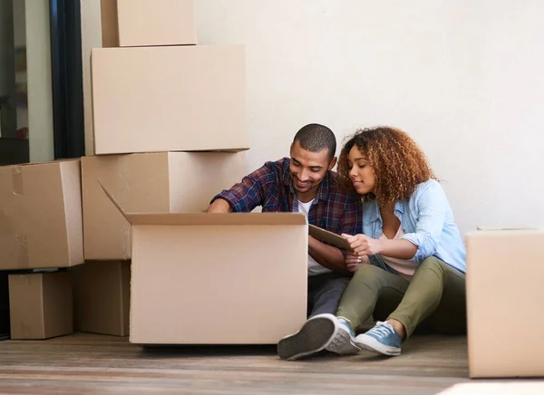 Was auch immer im Kasten ist. Aufnahme eines jungen Paares beim Auspacken einer Schachtel, während es auf dem Boden seines neuen Hauses sitzt. — Stockfoto