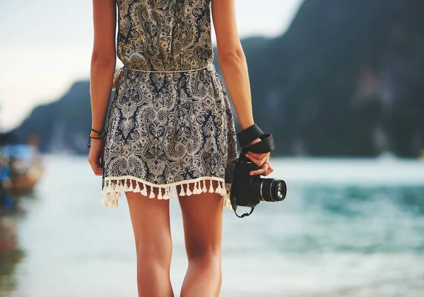 No moment goes uncaptured. Rear view shot of a young woman walking on the beach with a camera in hand. — Stock Photo, Image