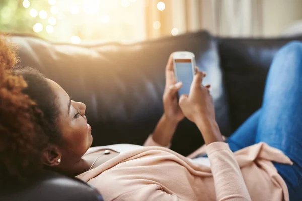 Vai com calma. Tiro de ângulo alto de uma jovem atraente usando seu celular enquanto relaxa em casa no sofá. — Fotografia de Stock