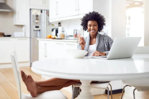 This is what Saturday morning looks like. Shot of a young woman surfing the net while enjoying breakfast in her kitchen at home. — Stock Photo, Image