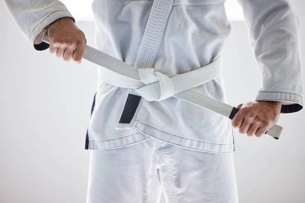 Prêt à commencer. Coupé coup d'un artiste martial masculin méconnaissable attachant sa ceinture dans la salle de gym. — Photo