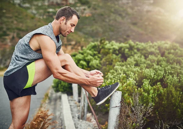 Amarrar os atacadores com força. Tiro de um jovem homem bonito treinando para uma maratona ao ar livre. — Fotografia de Stock