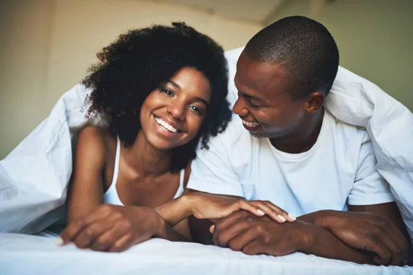 É difícil não ser feliz ao acordar para o amor. Retrato de um jovem casal feliz relaxando sob um edredom em seu quarto. — Fotografia de Stock